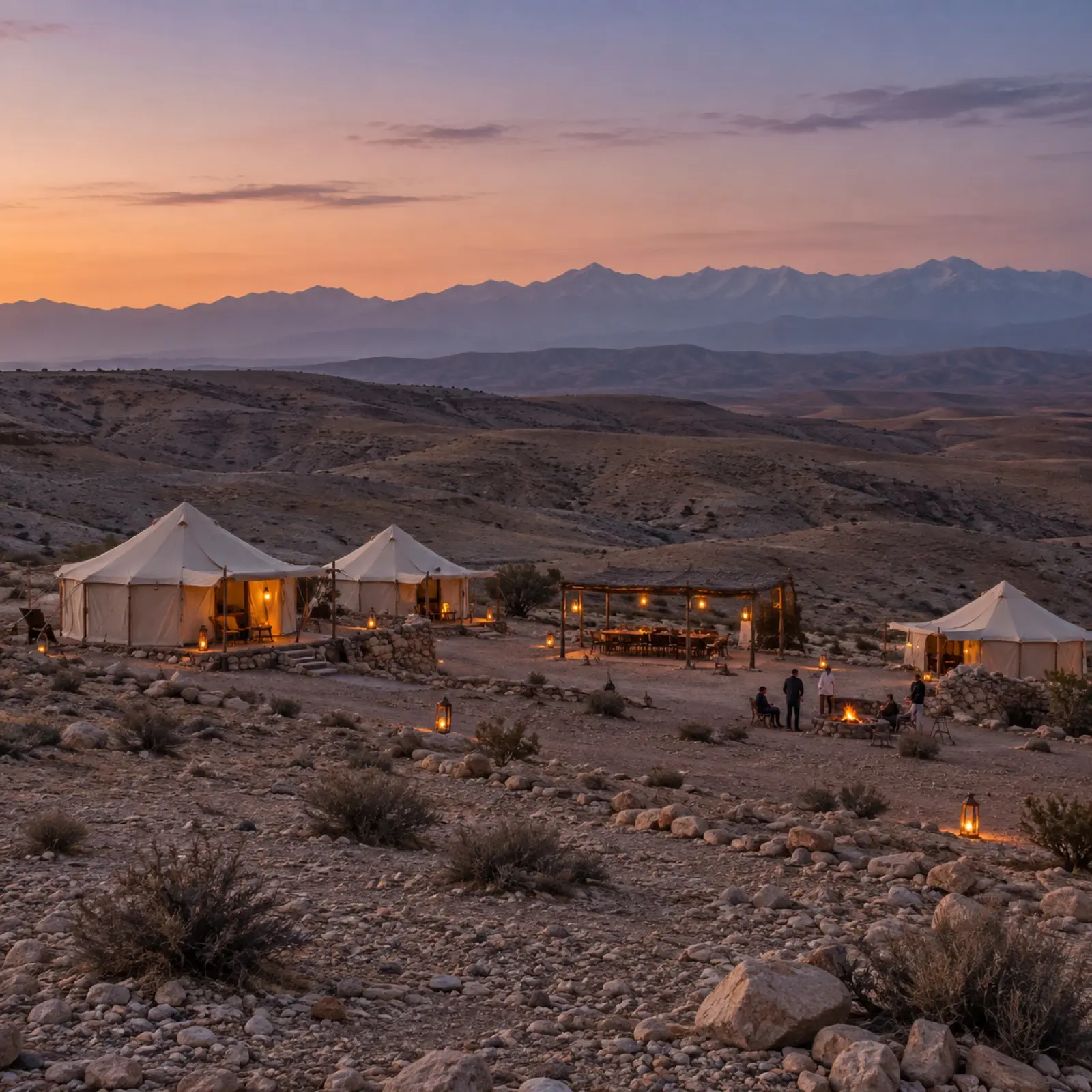 A desert camp in Agafay at dusk with the Atlas Mountains behind
