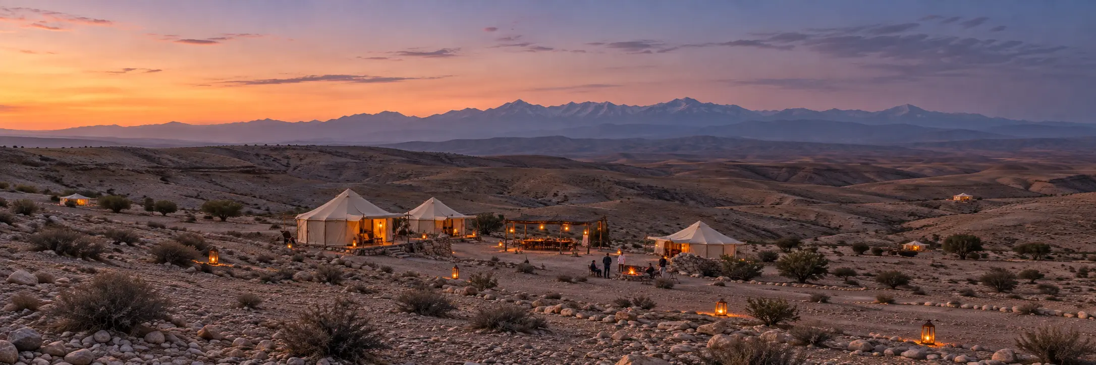 A desert camp in Agafay at dusk with the Atlas Mountains behind