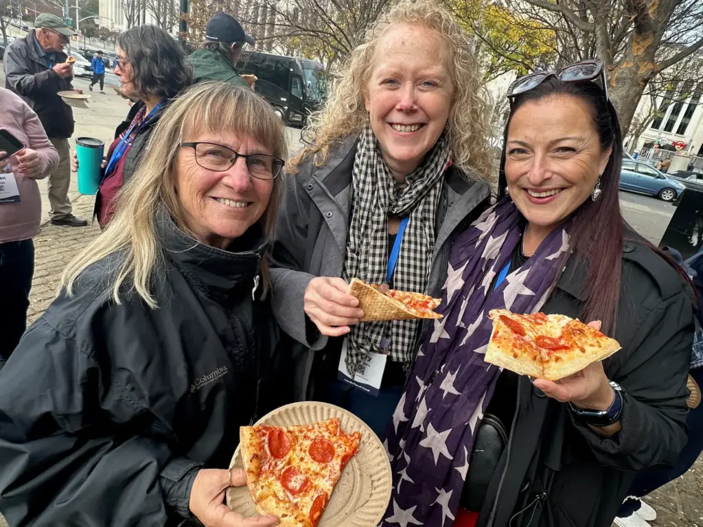 Three operators grinning over slices of pizza on a New York street