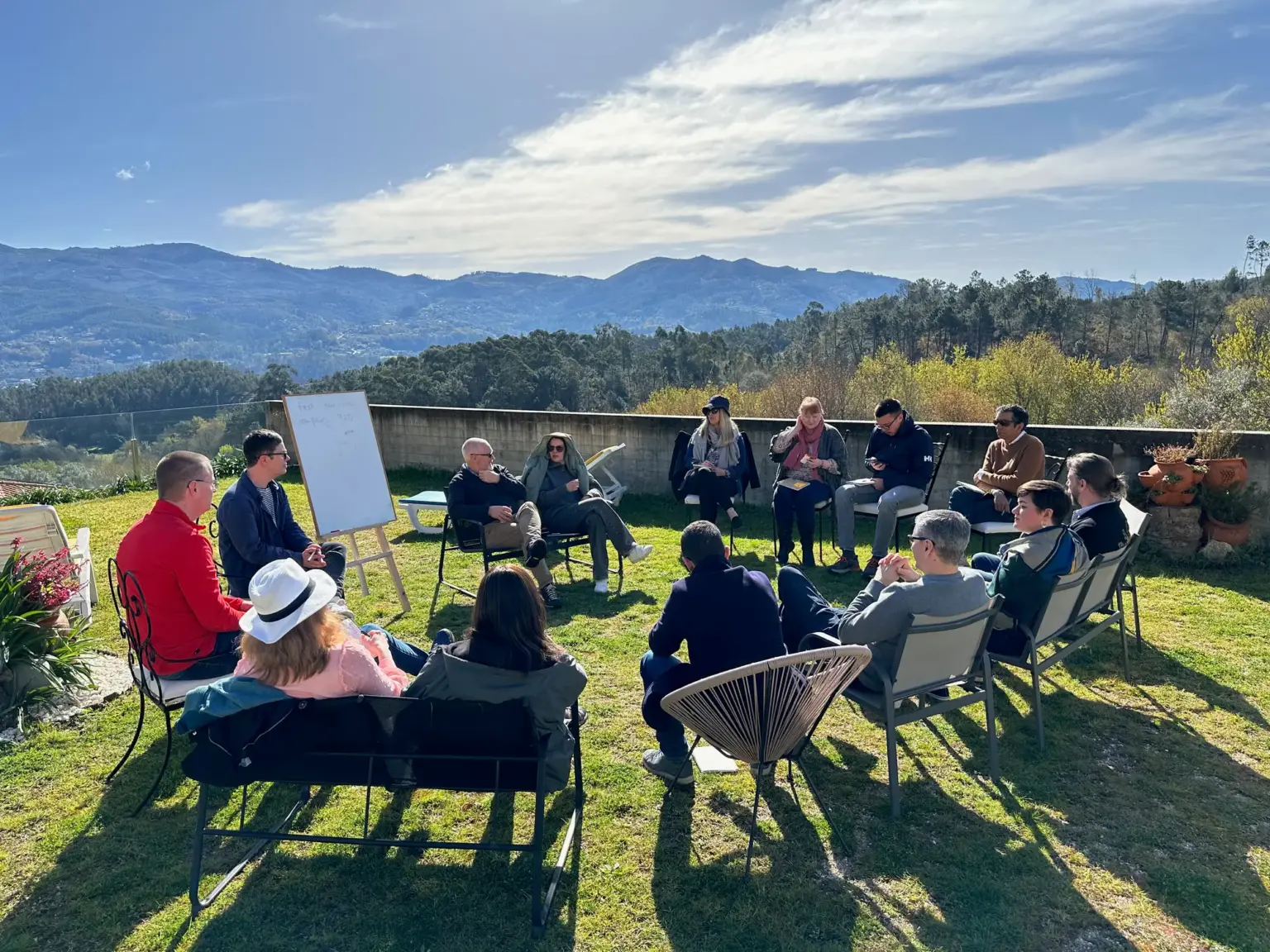 A Huddle group working in a circle on a lawn, with a whiteboard and mountains behind
